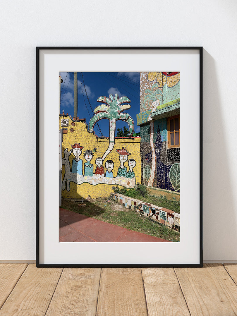 a photograph of a colorful mural with people and a palm tree on a yellow wall in Havana, Cuba.