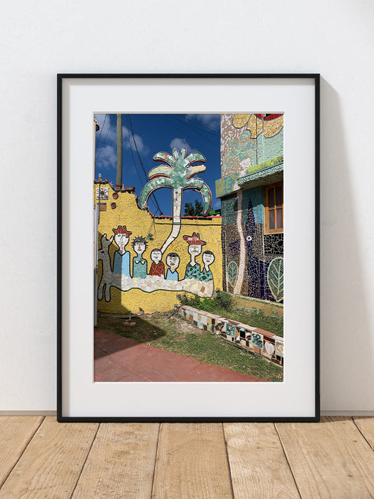 a photograph of a colorful mural with people and a palm tree on a yellow wall in Havana, Cuba.